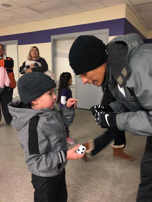 High School student signing mini soccer ball for PreK student High School student signing mini soccer ball for PreK student